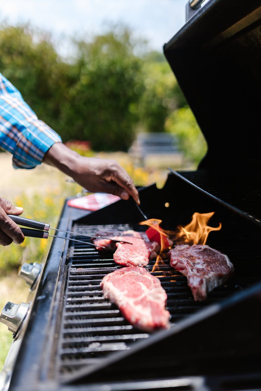 man in blue and white plaid shirt grilling meat