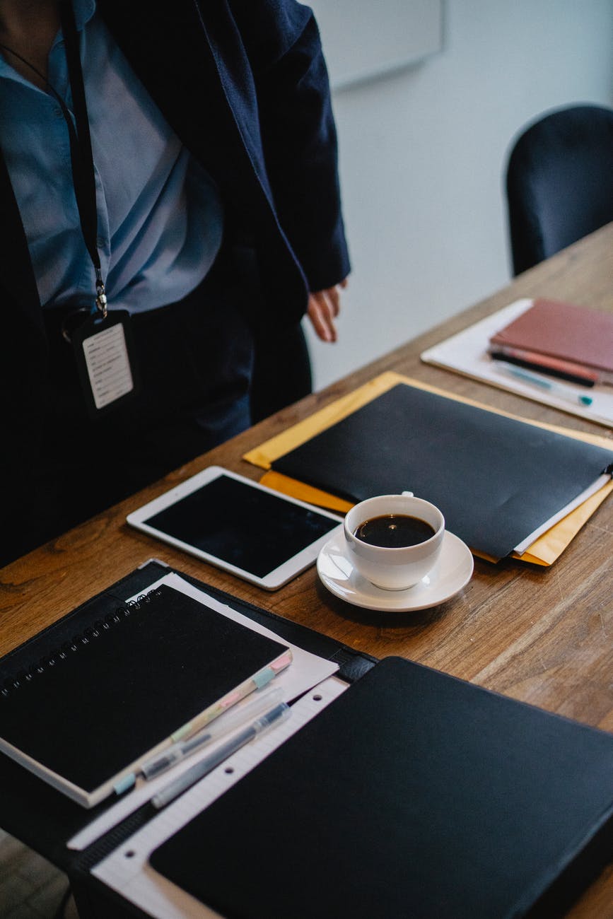 businessperson standing near table with cup of coffee and folders