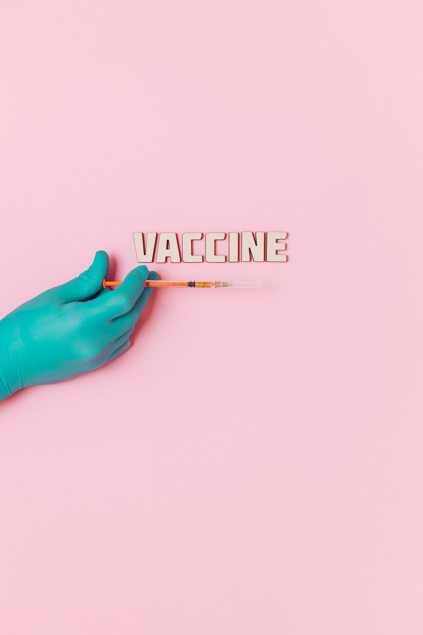 vaccine text and a person wearing latex glove while holding a syringe on pink background